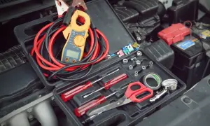Verktygslåda med startkablar, tångamperemeter och andra verktyg redo för att kontrollera plus och minus batteri i bilen.