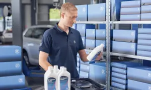 Mekaniker håller en flaska ZF Lifeguard Fluid 8, perfekt för att byta olja i automatlåda. Hyllor fyllda med ZF-produkter.