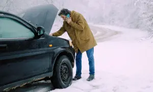 Man med telefon vid en bil med öppen motorhuv. Kallstart bil i snöväder.