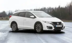Vit Honda Civic Tourer parkerad på en fuktig väg med träd i bakgrunden.