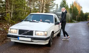 Vit Volvo med en tjej som öppnar dörren. En svensk registreringsskylt syns tydligt på bilen.