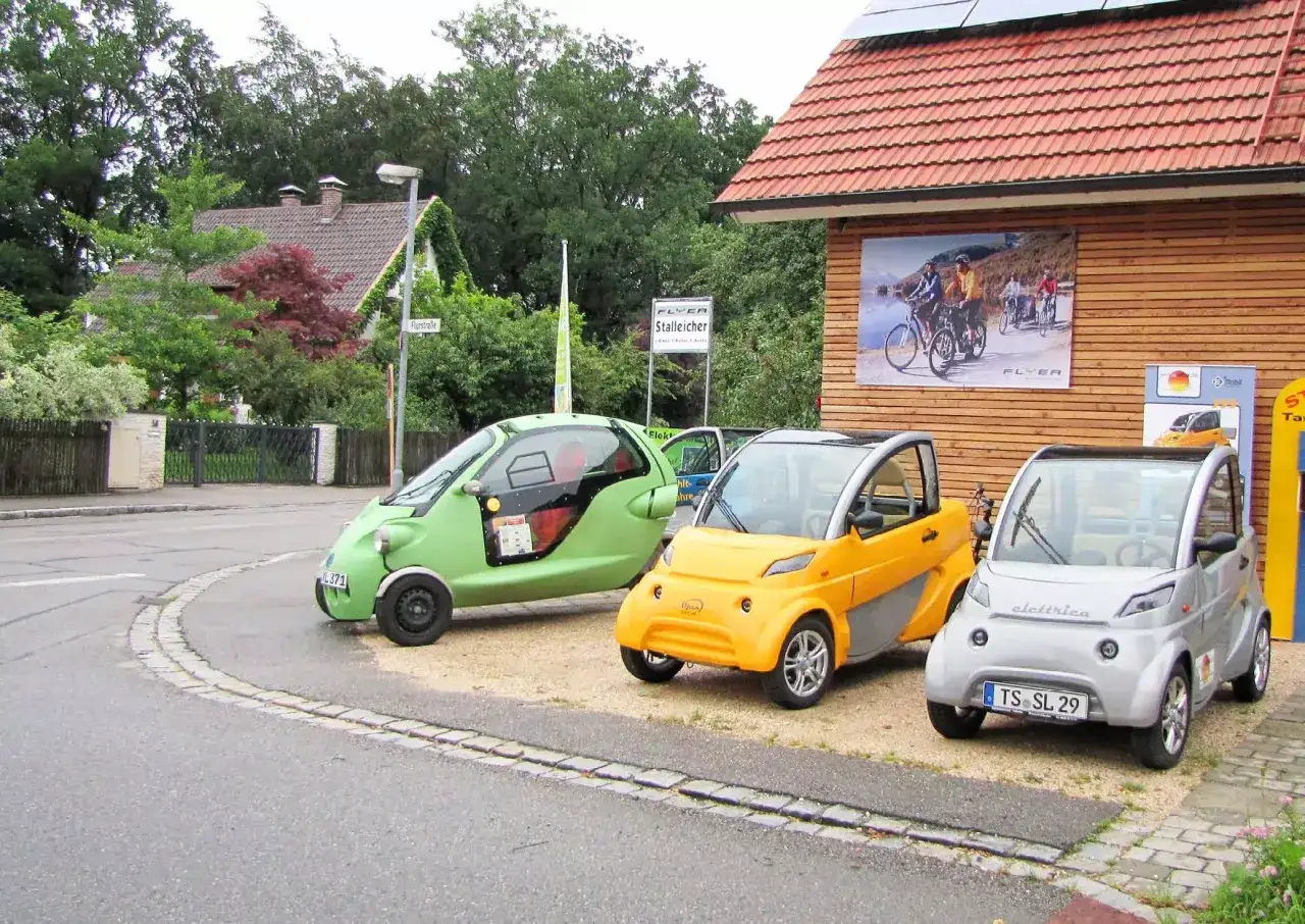 Tre små elbilar i olika färger står parkerade. En grön, en gul och en silverfärgad. Kanske en del av en volvo on demand-tjänst?