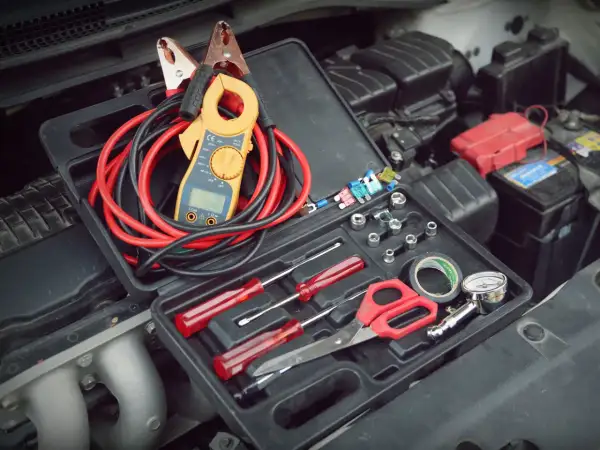 Verktygslåda med startkablar, tångamperemeter och andra verktyg redo för att kontrollera plus och minus batteri i bilen.