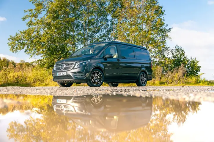 Mörkgrå Mercedes-Benz Vito med takhöjning, perfekt för service och äventyr. Reflekteras i en vattenpöl.
