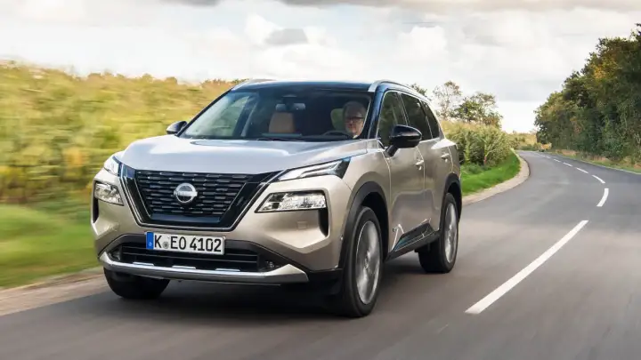 En man kör en beige Nissan X-Trail på en kurvig landsväg. Inga problem syns med bilen.